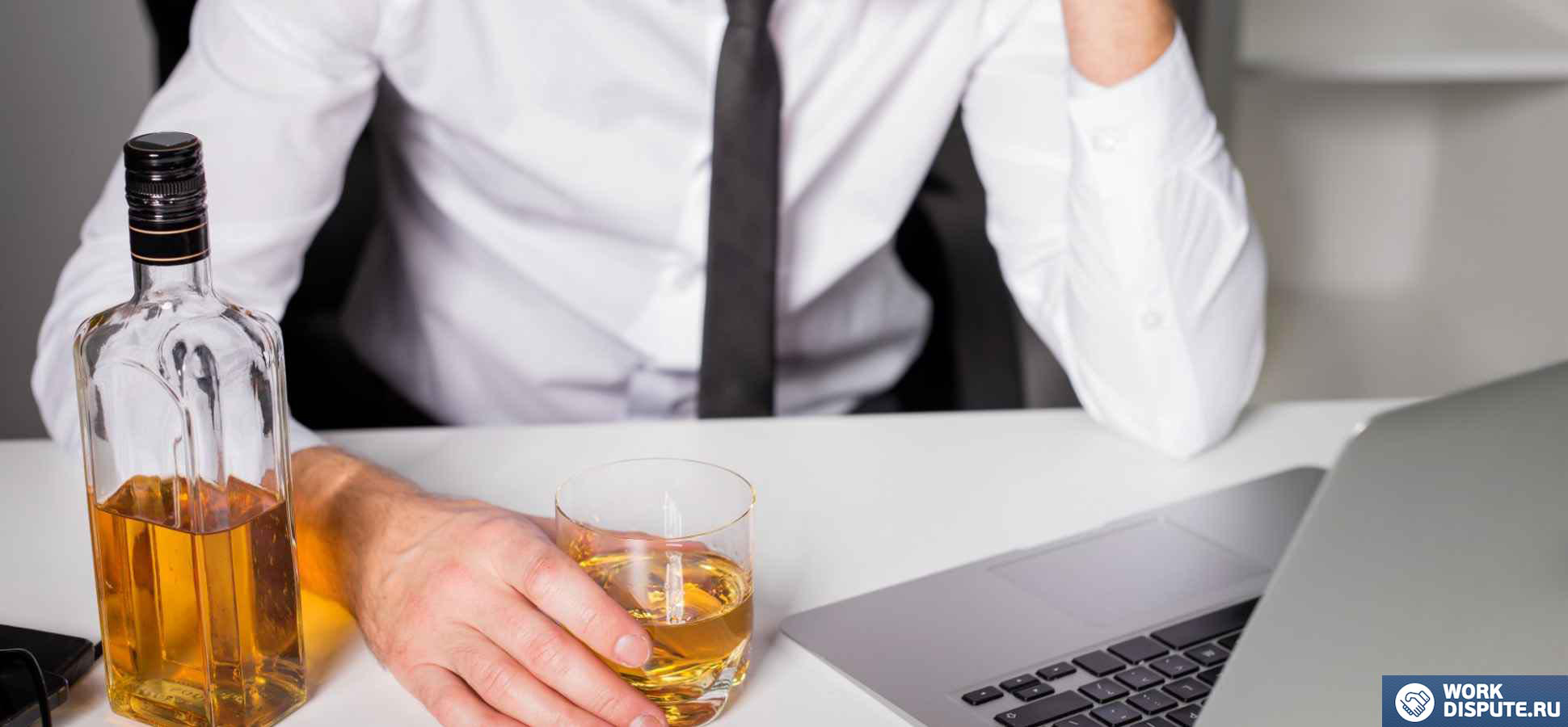 мужчина держит стакан с алкогольным напитком в руке за компьютером